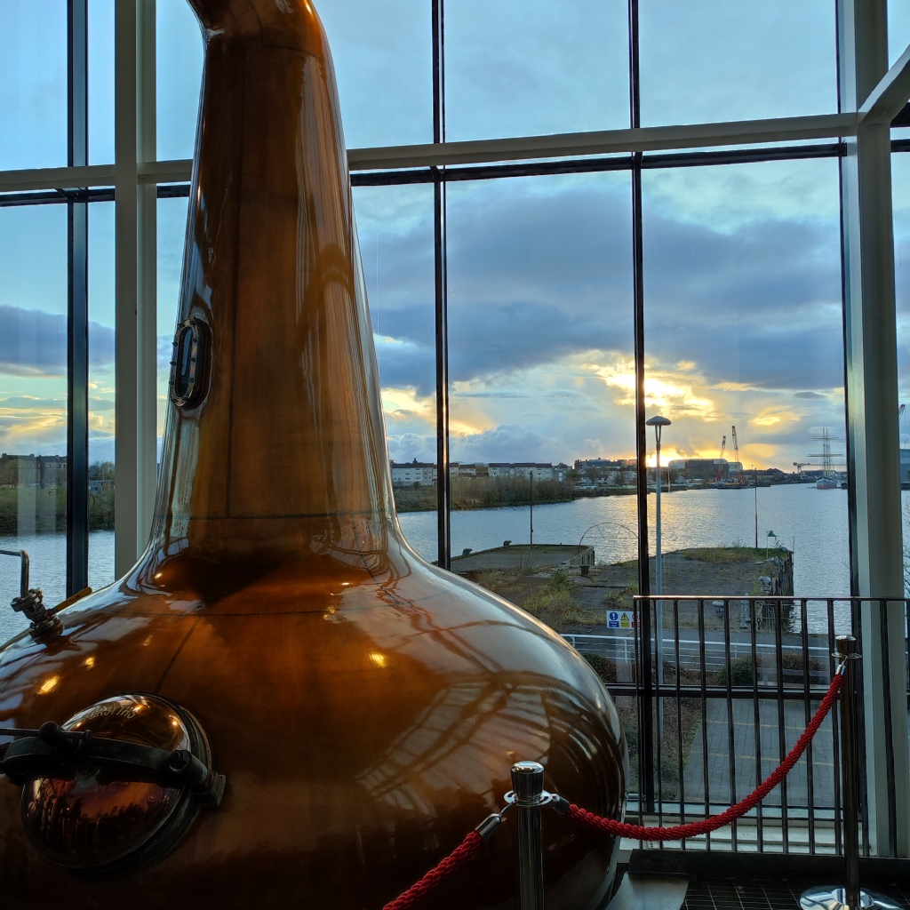 copper still in distillery, with window behind overlooking a river at dusk